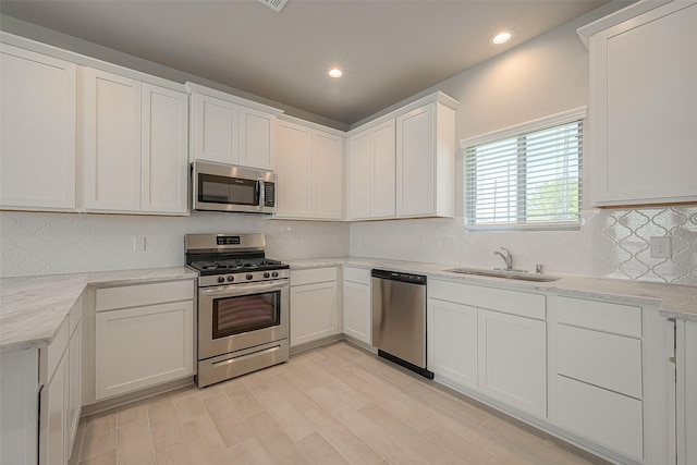 kitchen featuring light hardwood / wood-style flooring, tasteful backsplash, stainless steel appliances, white cabinets, and sink