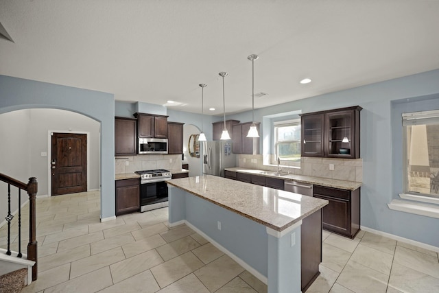 kitchen with glass insert cabinets, light stone counters, a center island, stainless steel appliances, and a sink