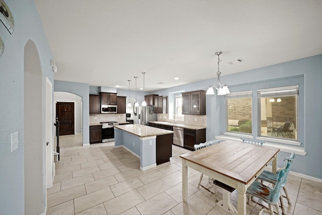 kitchen featuring dark brown cabinetry, stainless steel appliances, light countertops, a center island, and pendant lighting