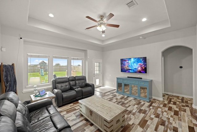 living area with arched walkways, a tray ceiling, plenty of natural light, and visible vents