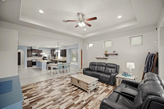 living room featuring a ceiling fan, a tray ceiling, light wood-style flooring, and recessed lighting