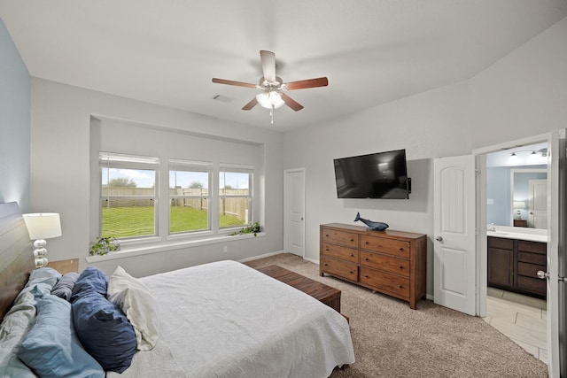 bedroom with light colored carpet, ceiling fan, visible vents, and ensuite bath