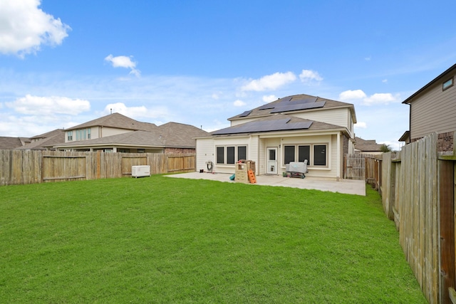 back of property featuring a yard, a fenced backyard, a patio, and solar panels