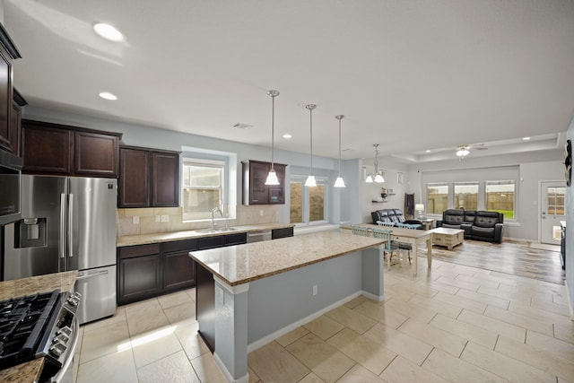 kitchen featuring light stone counters, open floor plan, hanging light fixtures, stainless steel appliances, and a sink