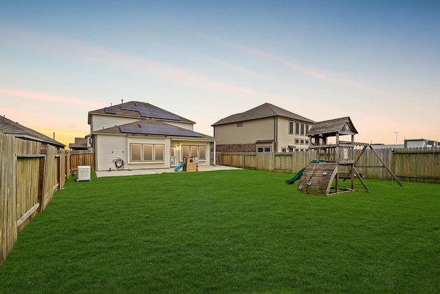 back of house at dusk featuring a playground, solar panels, a patio area, and a fenced backyard