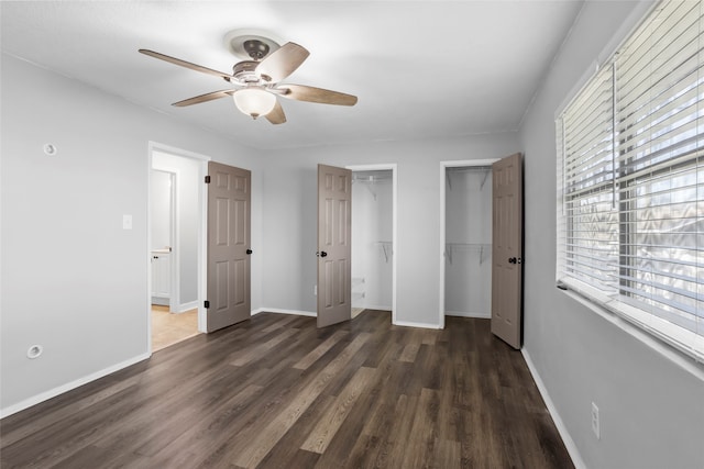 unfurnished bedroom featuring baseboards, multiple closets, wood finished floors, and a ceiling fan