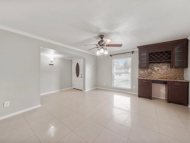 unfurnished living room with indoor bar, crown molding, ceiling fan, and light tile patterned floors