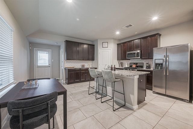 kitchen with appliances with stainless steel finishes, light tile patterned floors, an island with sink, and dark brown cabinetry