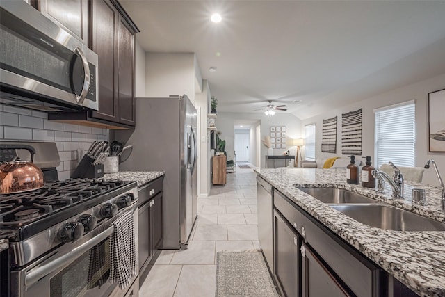 kitchen featuring appliances with stainless steel finishes, sink, light tile patterned floors, light stone countertops, and dark brown cabinetry