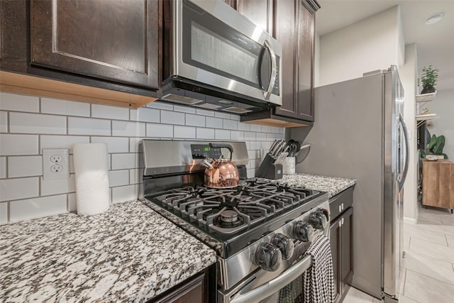 kitchen featuring dark brown cabinets, decorative backsplash, stainless steel appliances, and light stone counters