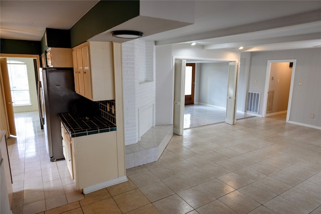 kitchen with tile countertops, light brown cabinets, light tile patterned flooring, and stainless steel fridge