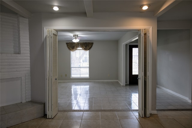 spare room with a fireplace, beamed ceiling, ceiling fan, and light tile patterned floors