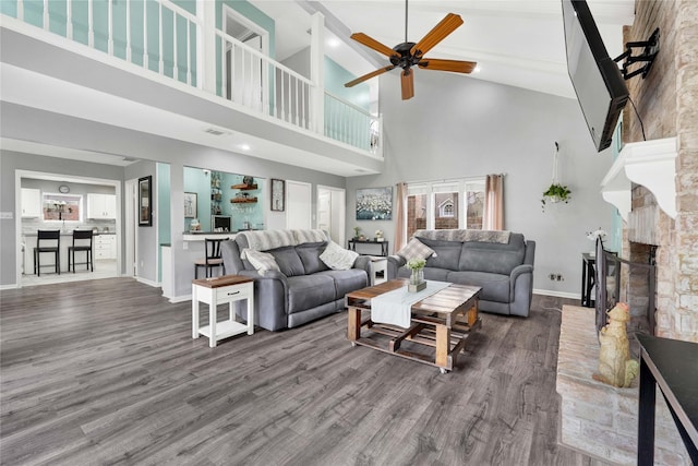 living room featuring ceiling fan, a fireplace, baseboards, and wood finished floors