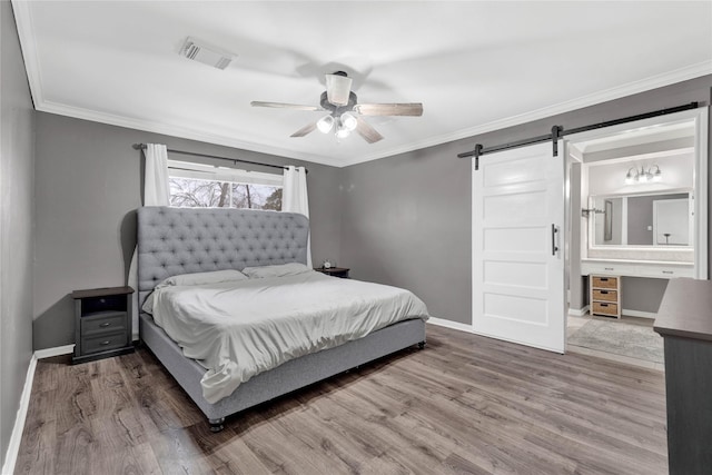 bedroom featuring ornamental molding, a barn door, wood finished floors, and visible vents