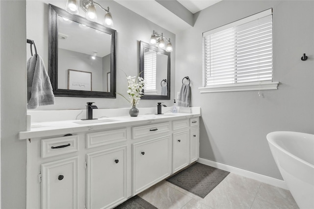 bathroom featuring double vanity, a sink, tile patterned flooring, a freestanding tub, and baseboards