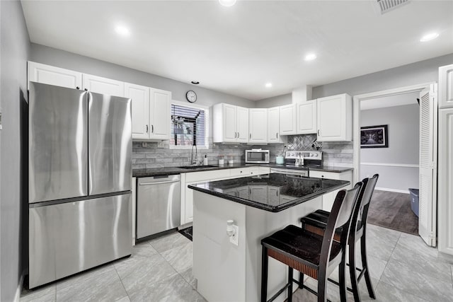 kitchen with a center island, appliances with stainless steel finishes, white cabinetry, a sink, and a kitchen breakfast bar