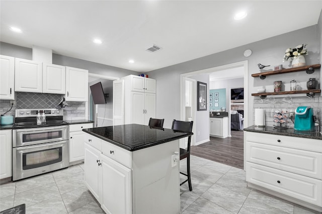 kitchen with range with two ovens, a kitchen island, a breakfast bar, and white cabinetry