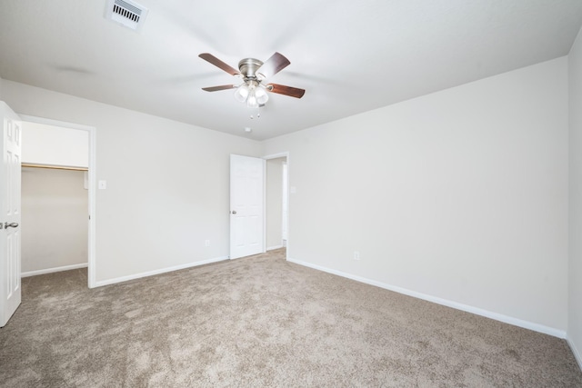 unfurnished bedroom featuring ceiling fan, a closet, a walk in closet, and carpet flooring