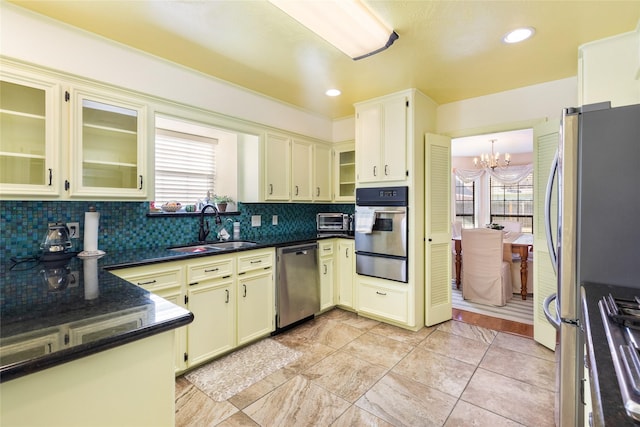 kitchen featuring dark stone countertops, a notable chandelier, sink, backsplash, and appliances with stainless steel finishes