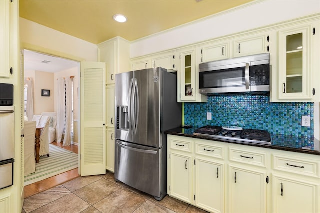 kitchen with dark stone countertops, appliances with stainless steel finishes, backsplash, and cream cabinets