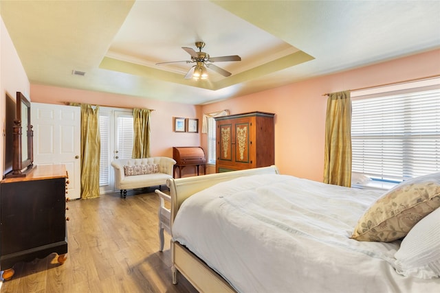 bedroom with a raised ceiling, multiple windows, light hardwood / wood-style flooring, and ceiling fan