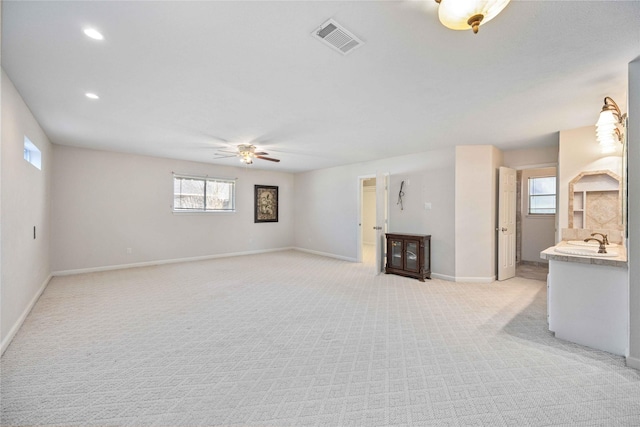 unfurnished living room featuring ceiling fan, sink, and light colored carpet