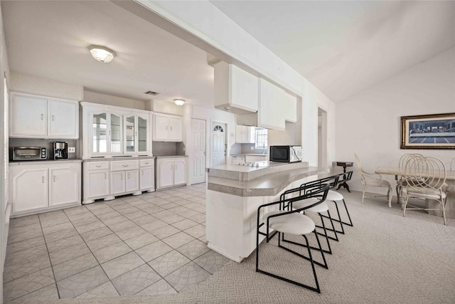 kitchen featuring lofted ceiling, light tile patterned floors, a kitchen breakfast bar, kitchen peninsula, and white cabinets