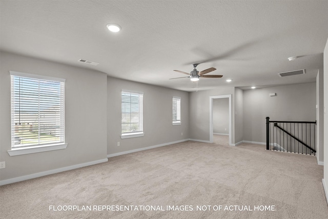 spare room with a textured ceiling, light carpet, and ceiling fan