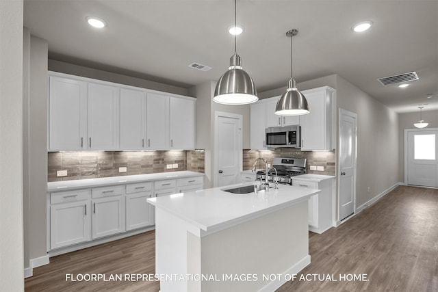 kitchen with a center island with sink, appliances with stainless steel finishes, sink, white cabinets, and hanging light fixtures