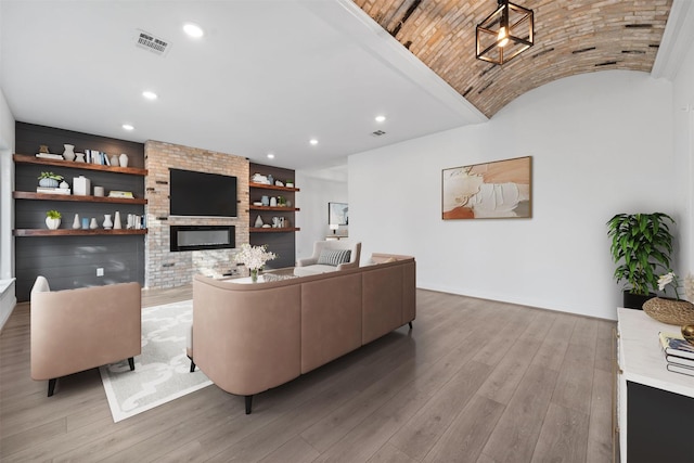 living area with built in shelves, a fireplace, visible vents, light wood-style floors, and baseboards