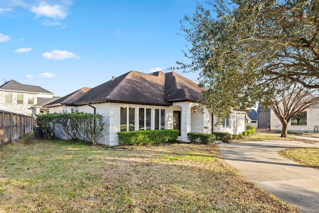 view of front of property with brick siding, a front yard, fence, and a shingled roof