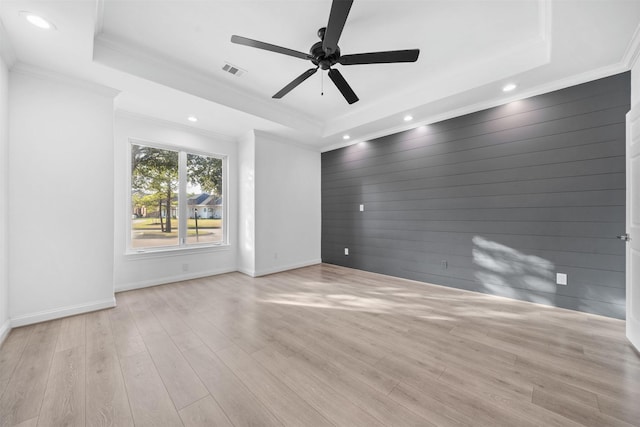 spare room with light wood finished floors, a tray ceiling, and visible vents