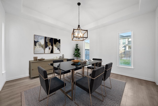 dining space with an inviting chandelier, a raised ceiling, baseboards, and wood finished floors