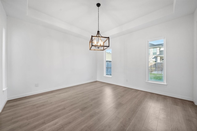 unfurnished room featuring a raised ceiling, a notable chandelier, baseboards, and wood finished floors