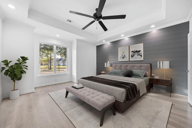 bedroom featuring light wood-type flooring, a raised ceiling, visible vents, and crown molding