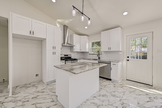 kitchen featuring stainless steel appliances, wall chimney range hood, pendant lighting, a kitchen island, and white cabinetry