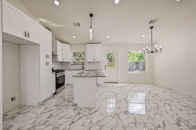 kitchen with white cabinets, stainless steel gas range oven, a kitchen island, and light stone counters