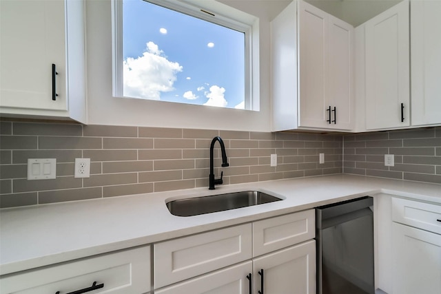 kitchen with stainless steel dishwasher, white cabinets, a sink, and tasteful backsplash