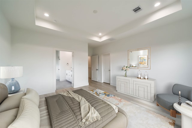 bedroom featuring a raised ceiling, recessed lighting, ensuite bathroom, wood finished floors, and visible vents