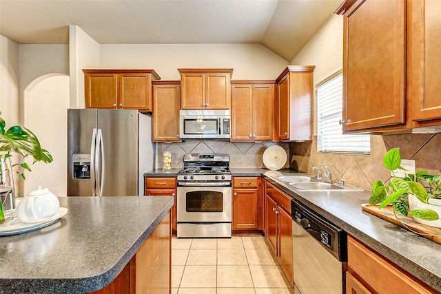 kitchen featuring appliances with stainless steel finishes, vaulted ceiling, backsplash, light tile patterned floors, and sink