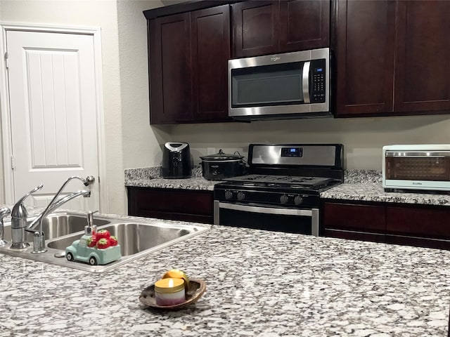 kitchen featuring sink, dark brown cabinets, light stone countertops, and stainless steel appliances