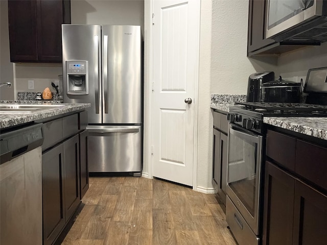 kitchen featuring light hardwood / wood-style flooring, sink, stone countertops, stainless steel appliances, and dark brown cabinets