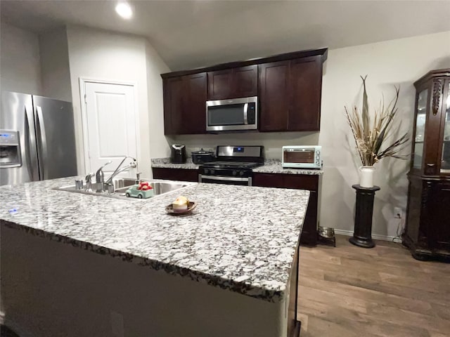 kitchen with dark brown cabinets, sink, stainless steel appliances, and a kitchen island with sink