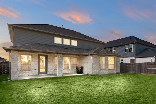 back house at dusk featuring a patio area and a yard