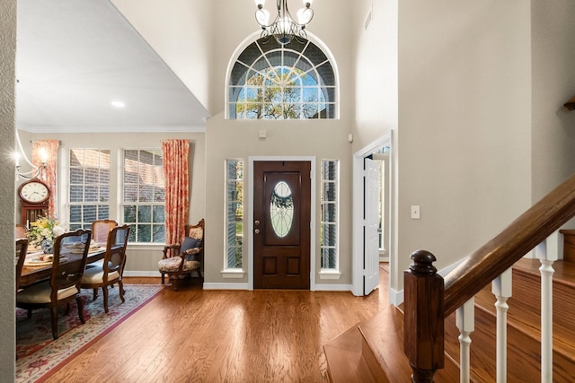 entryway featuring a chandelier, crown molding, wood-type flooring, and a towering ceiling