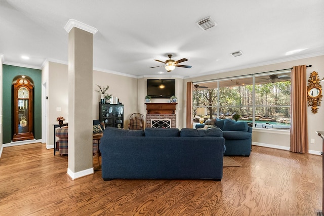 living room with hardwood / wood-style flooring, ceiling fan, ornamental molding, and a fireplace