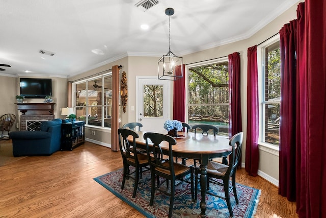 dining area with a brick fireplace, crown molding, an inviting chandelier, and wood-type flooring