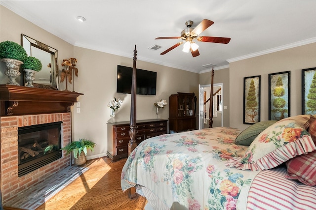 bedroom with ceiling fan, ornamental molding, a brick fireplace, and hardwood / wood-style floors