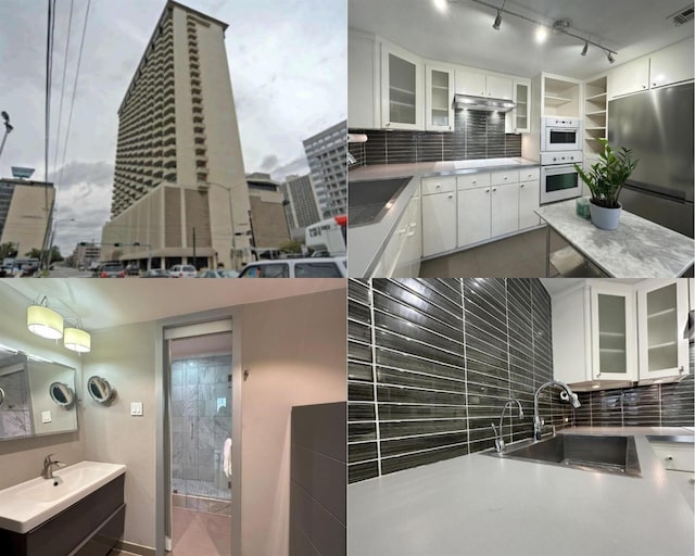 kitchen with stainless steel refrigerator, decorative backsplash, under cabinet range hood, and a sink