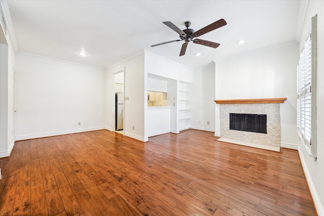 unfurnished living room featuring built in features, hardwood / wood-style floors, crown molding, and ceiling fan